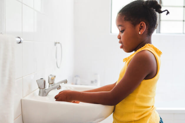 Niño lavándose las manos en el lavabo, aprendiendo hábitos de higiene esenciales para mantenerse protegido. 